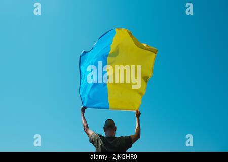 un homme, vu de l'arrière, fait passer le drapeau ukrainien au-dessus de sa tête dans le ciel par une journée ensoleillée Banque D'Images
