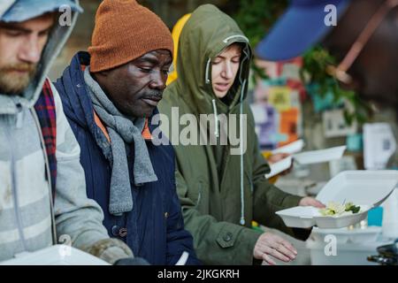Groupe de sans-abri en vêtements chauds venant manger gratuitement des dons de nourriture par des bénévoles de la communauté caritative Banque D'Images