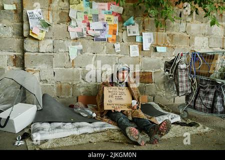 Homme sans-abri assis sur le sol avec le signe et le verre pour l'argent et mendiant pour les aumône Banque D'Images