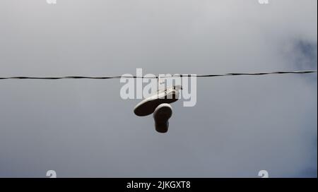 A low angle shot of old pair of shoes hanging on a rope against a cloudy sky Stock Photo