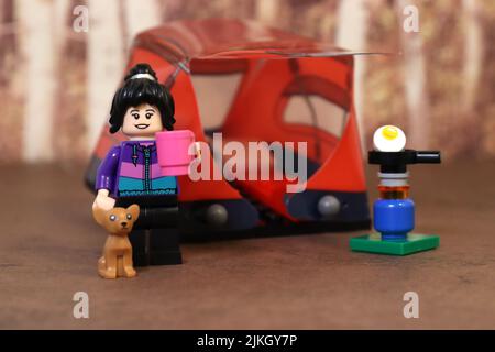 Mini figure, personnage femelle jouet tenant une tasse de café avec chien, camping dans la forêt. Banque D'Images