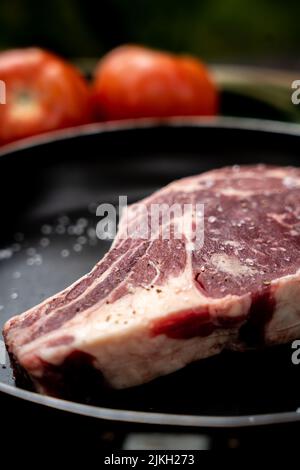 A piece of raw beef steak on a bone with tomatoes and spices Stock Photo