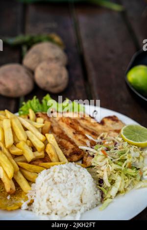 A beautiful shot of chicken, fries, rice and cabbage salad in a plate Stock Photo