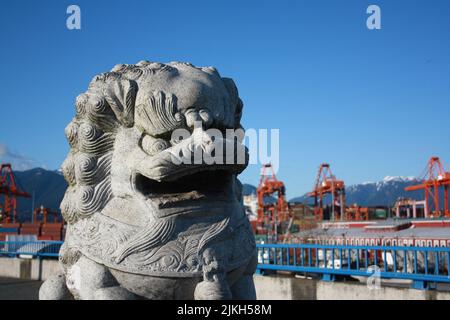 The Chinese lion sculpture with a the mountains and cranes in the Port of Vancouver, British Columbia, Canada Stock Photo