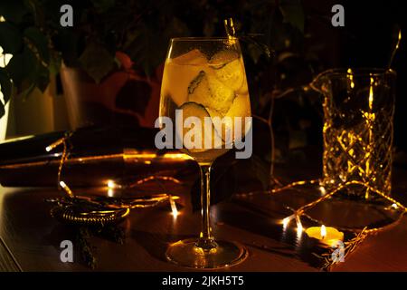 A closeup of a cucumber gin tonic cocktail in a wine glass decorated with candles and lights Banque D'Images
