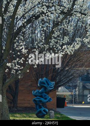 A vertical shot of a sculpture at the Olathe Kansas City building and a blooming pear tree Stock Photo