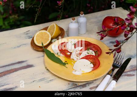 Un gros plan d'une salade italienne Caprese sur une assiette jaune à côté des couverts sur un fond en bois Banque D'Images