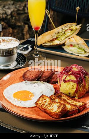 A vertical closeup of a Dominican breakfast with an egg and fried meat, and sandwiches on a terrace Stock Photo