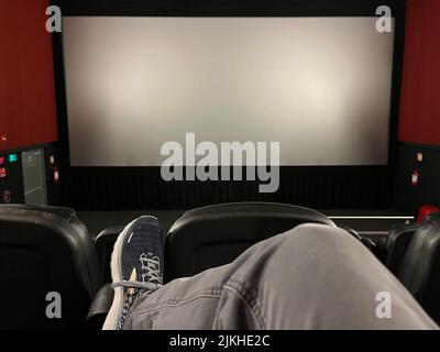 Du point de vue d'un gardien de cinéma, nous voyons sa jambe et sa chaussure croisées pendant qu'il se détend dans un cinéma vide, regardant un écran vide jusqu'au début du film Banque D'Images