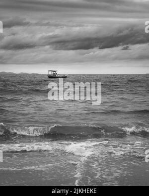 A vertical grayscale shot of the tranquil waves washing the sandy beach Stock Photo