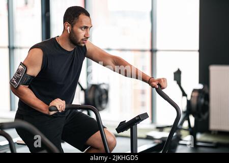 Jeune homme noir sportif utilisant un vélo elliptique pendant l'entraînement à la salle de gym Banque D'Images