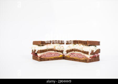 A pastrami sandwich sliced in half portraying all of its ingredients on a white background Stock Photo