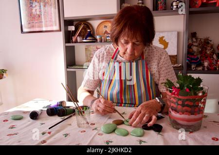 Une femme caucasienne mûre peignant des pierres avec des peintures acryliques sur la table à la maison à Barcelone, Espagne Banque D'Images