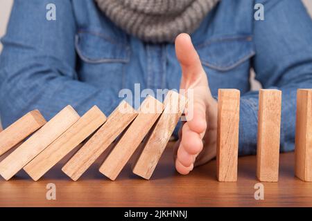 A closeup of a human hand stopping wooden domino blocks from falling on a table Stock Photo