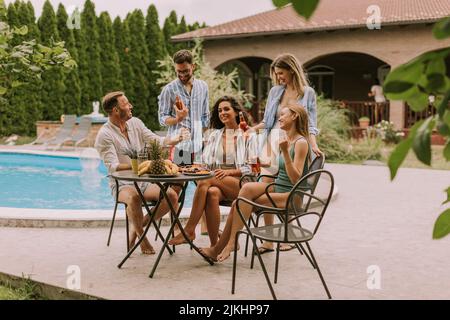 Groupe de jeunes heureux qui applaudissent au cidre près de la piscine dans le jardin Banque D'Images