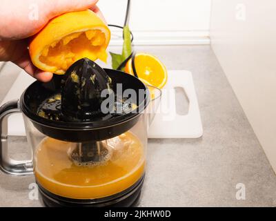 homme pressant des fruits d'orange frais à la centrifugeuse. Préparer un petit déjeuner sain à partir d'ingrédients naturels. Boisson à base de vitamines organiques Banque D'Images