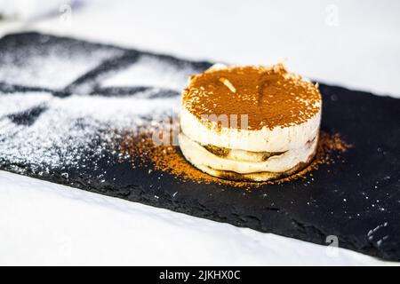 A tiramisu dessert served on a black flat stand on a blurred background Banque D'Images