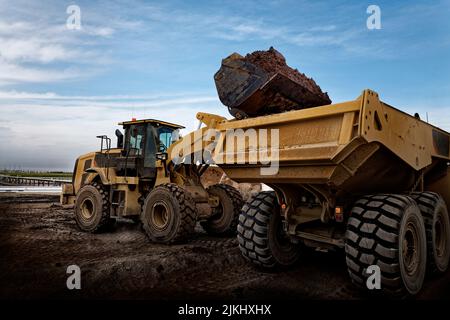 A number of dump trucks loaded with dirt in the cloudy sky background Stock Photo