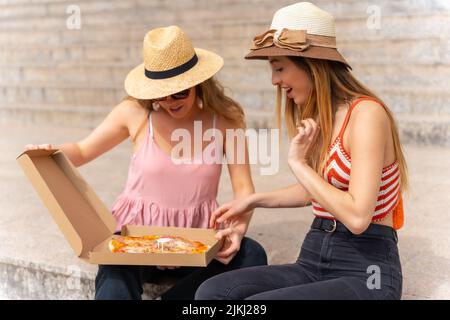 Amis mangeant de la pizza dans la ville appréciant les vacances, un des amis très heureux d'ouvrir la boîte à pizza Banque D'Images