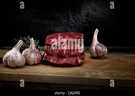 The magnetic close-up studio shot with  fresh slices of thick steak meat with garlic and rosemary on a wooden board Stock Photo