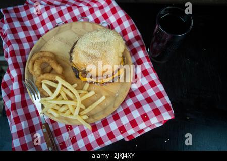 An angle top shot of a burger on a plate with onion rings and french fries on the side. Stock Photo