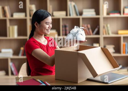 Bonne jeune femme chinoise ouvre une boîte en carton et regarde les baskets, profitez de vos achats à l'intérieur de la chambre Banque D'Images