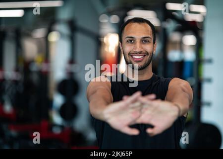 Beau sourire Noir Homme étirant les bras avant l'entraînement dans la salle de gym Banque D'Images