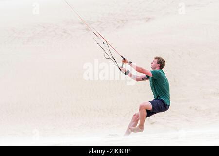 Jeune homme manipulant 4 lignes barre de contrôle d'un entraîneur de vol de quatre lignes parafoil / 4 lignes stunt kite sur la plage de sable dans le vent fort en été Banque D'Images