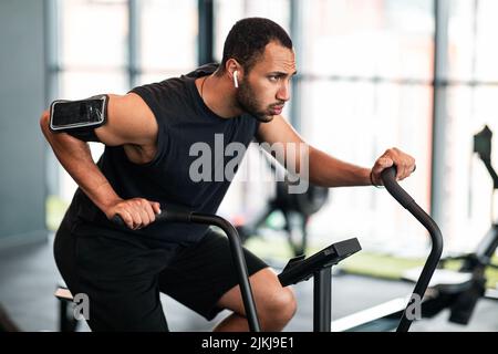 Black Man motivé faisant de l'entraînement cardio avec machine elliptique de vélo à la salle de gym Banque D'Images