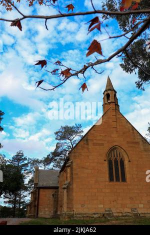 A vertical shot of the Holy Trinity Anglican Church with some red leaves in the foreground, Berrima Southern Highlands, NSW, Australia Stock Photo