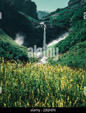 A vertical shot of a waterfall flowing among the high wooded mountains Stock Photo