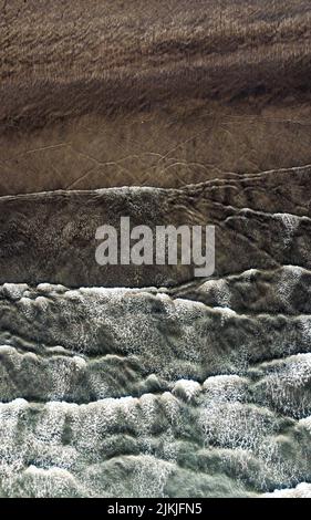 A vertical drone shot of the foamy waves of the sea touching the sandy shore, Murud Janjira, India Stock Photo