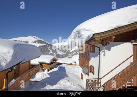 A scenic view of wooden houses covered with snow on the slopes of mountains on a sunny day Stock Photo