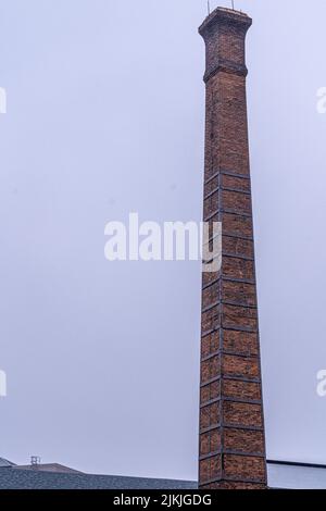 A vertical shot of a tall chimney tower made of red brick rising to the sky on a gloomy day Stock Photo