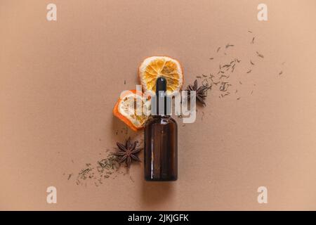 Un flacon compte-gouttes en verre brun d'huile essentielle d'agrumes avec des tranches d'orange séchées, de l'anis étoilé et des épices Banque D'Images