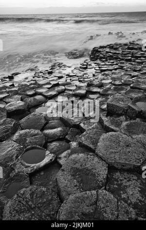 A vertical grayscale shot of the water washing basalt rocks at the Giants Causeway in Northern Ireland Stock Photo