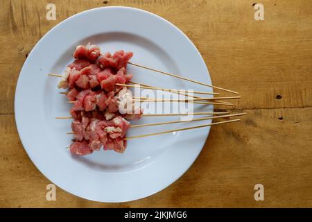 Satay de chèvre cru sur plaque blanche avec table en bois Banque D'Images