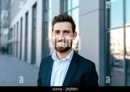 Portrait d'un homme d'affaires millénaire souriant et confiant avec une barbe en costume regardant l'appareil photo Banque D'Images