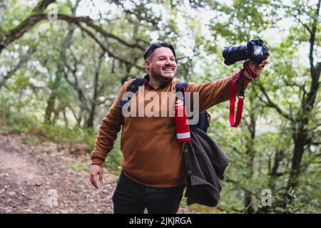 Un homme caucasien souriant prenant un selfie avec un appareil photo professionnel dans la forêt Banque D'Images