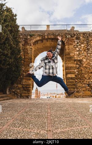 Photo verticale d'un jeune homme dans une chemise à carreaux sautant dans la joie près d'un pont historique Banque D'Images