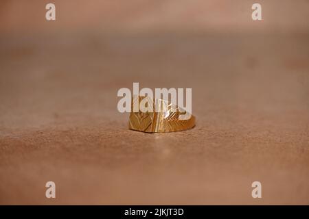 gros plan la belle bague dorée garder sur la table brune sur un arrière-plan rouge marron hors foyer. Banque D'Images