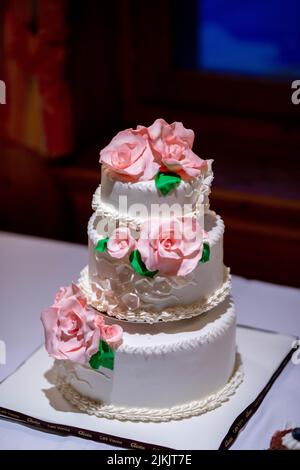 Un gros plan vertical du gâteau de mariage blanc traditionnel de trois étages avec roses roses roses Banque D'Images