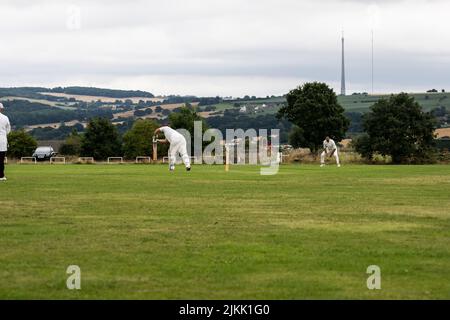 Batteur jouant un tir défensif avant lors d'un match de cricket du village local avec Emley Moor transmission Mast en arrière-plan dans le Yorkshire Banque D'Images