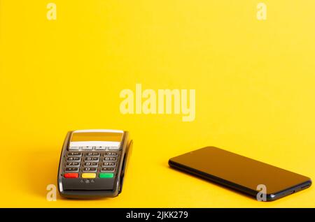 A closeup shot of the POS terminal credit card machine and a phone on a yellow background Stock Photo