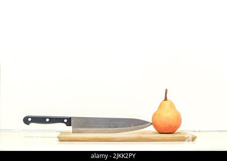 A beautiful shot of a big knife toughing a ripe pear on a wooden kitchen board with isolated white background Banque D'Images