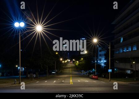 A beautiful shot of an empty street with parked cars and lighting street lamps at night in Arkansas, United States Stock Photo