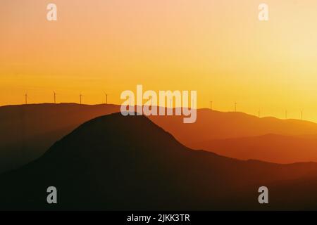 Une silhouette d'un temps brumeux sur les montagnes au coucher du soleil avec des moulins à vent sur le dessus Banque D'Images