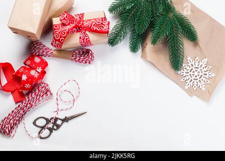 L'emballage présente un arrière-plan.Bricolage créatif passe-temps, moderne boîte cadeau de noël dans le papier artisanal élégant avec ruban rouge.Vue de dessus table blanche avec sapin Banque D'Images
