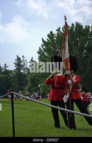 A vertical shot of two royal guides holding a flag and standing on a green grass in a park in Canada Stock Photo