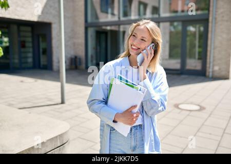 Jeune fille souriante étudiante à l'université parlant au téléphone à l'extérieur du campus. Banque D'Images